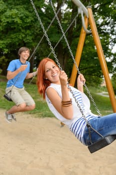 Laughing teenage couple on swing in park have fun together