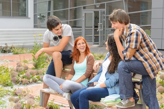 Student friends sitting on bench outside university campus laughing chatting