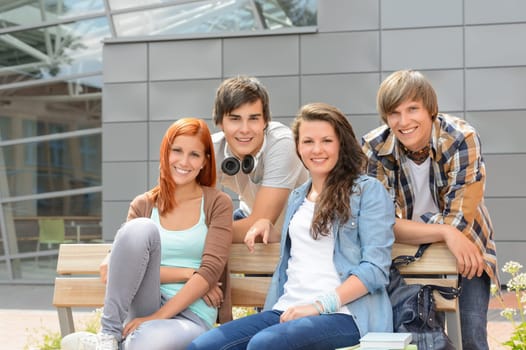 Students friends sitting bench outside campus smiling at camera