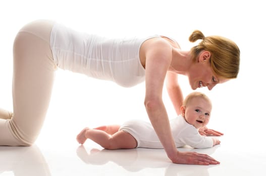 Young mother does back-education gymnastics with her 6-month-old daughter,isolated against a white background. She kneels on the ground and makes a lie over the baby.