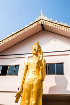 Standing bronze buddha image statue in front of monk school building