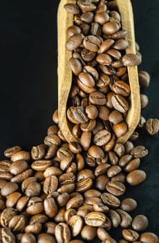 View of Roasted coffee beans on a rich textured surface in Wooden coffee scoop on Black background. Enjoy your morning coffee for living, use it as your Copy space, Design, Wallpaper and Poster, Selective focus.