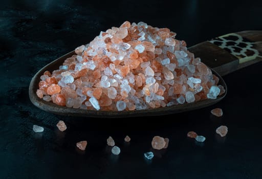 View of Pink Himalayan Salt with Bright colors textured surface in Wooden scoop on Balck background. Crystals and crushed blocks of natural pink salt, Chipped Himalayan salt stone, use it as your Space for text, Design, Wallpaper and Poster, Selective focus.