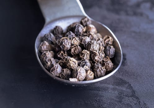 Raw organic black peppercorns or Dry black pepper seeds in stainless steel spoon on Dark background. use it as your Copy space, Design, Wallpaper and Poster, Selective focus.