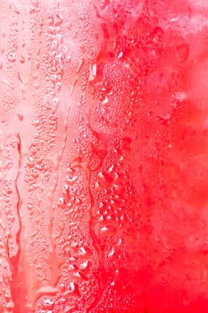 Glass surface of red drink with ice cubes background
