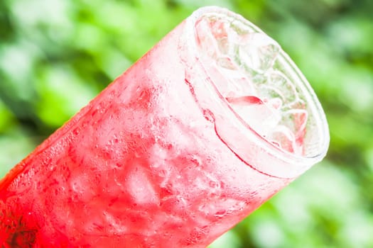 Cold glass of sweet red drink with ice cubes