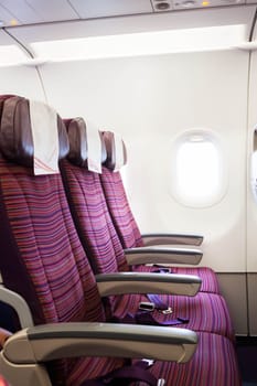 Airplane seat row in passenger cabin with window beside