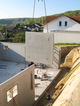 Construction of a prefabricated cellar with a concrete wall hanging from a crane.