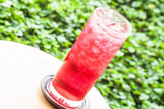 Glass of iced sweet red drink on green background