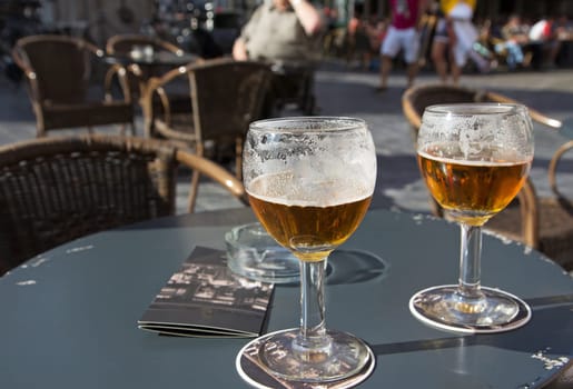 Close up view of two glasses of Belgian beer standing on the table on pub front garden. All potential trademarks are removed.