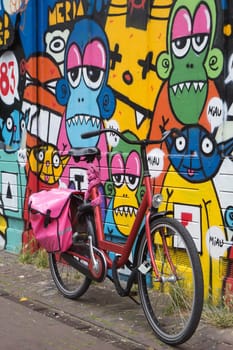 The bicycle leaning against a wall painted with color pictures and inscriptions. (Amsterdam, Netherlands). All potential trademarks are removed.