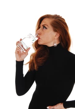 A middle aged woman in a black dress standing in profile isolated on.white background, drinking a glass of water..