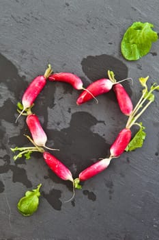 Fresh radishes in heart shape on slate plate