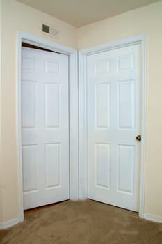 View of two white interior doors one closed, the other is ajar or slightly open in carpeted room.