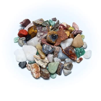 A pile of many different size, shape and colored tumbled stones, shot over white surface.