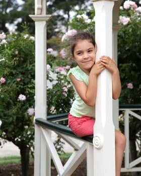 Pretty girl hugging a gazebo pole, with flower bushes in background