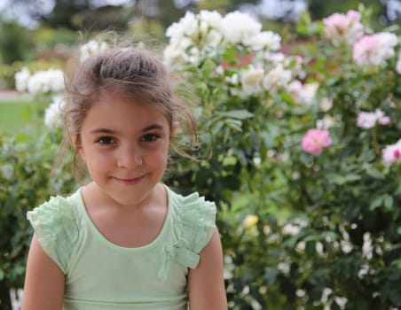 Cute little girl smiling and looking at camera, with rose bushes in the background