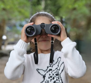 Little girl in white jumper looking through binoculars