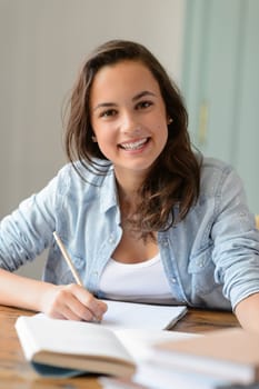 Teenage student girl studying at home smiling at camera