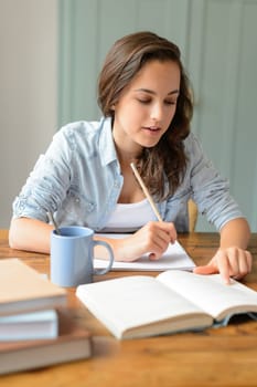 Teenage student girl studying book at home sitting behind table