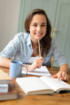 Student teenage girl studying at home sitting behind table smiling