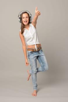 Girl enjoy listening music and dance thumb-up full length on gray