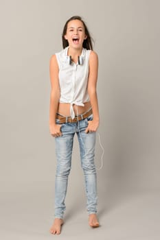 Singing teenage girl with headphones full length on grey background