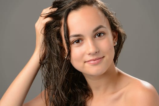 Teenage girl touch wet hair care cosmetics on gray background