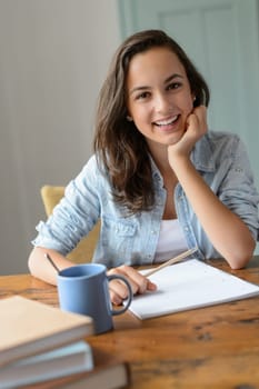 Teenage student girl studying at home smiling leaning against table