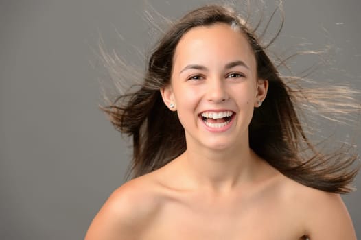 Laughing teenage girl blowing hair beauty skin on gray background