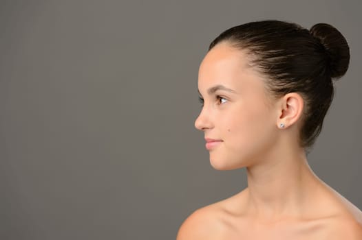 Teenage girl skin care cosmetics looking away side view on grey background