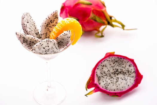 White pulp of half a pitaya cut into wedges and presented in a glass. The decorative mandarine slice is also complementing the pitaya's flavor..