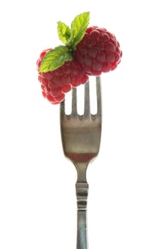 Raspberries with peppermint on a fork in the backlight