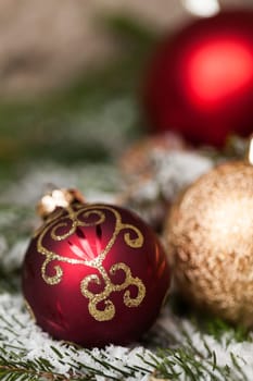red Christmas baubles between cones and fir branches covered with snow as macro detail