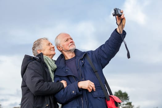 older adult couple seniors happy to take self-portrait photograph with digital camera on vacation