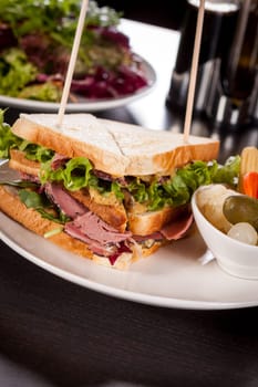 Delicious sandwich clubsandwich with bacon ham cheese and one with mixed pickels on a plate