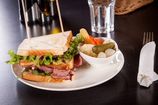 Delicious sandwich clubsandwich with bacon ham cheese and one with mixed pickels on a plate
