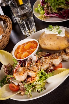 Roasted shrimp on a skewer on a mixed salad with dipp and foil potato on a plate