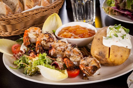 Roasted shrimp on a skewer on a mixed salad with dipp and foil potato on a plate