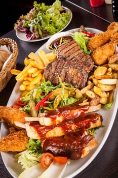 Huge barbecue plate with mixed meat and steaks on salad