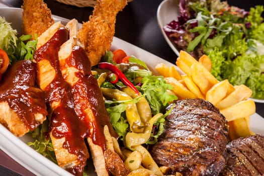 Huge barbecue plate with mixed meat and steaks on salad