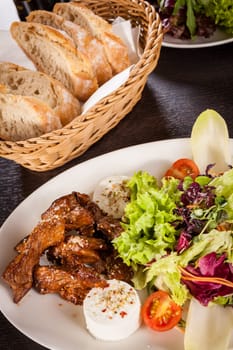 Fresh salad with fresh goat cheese and fried beef strips served on a plate