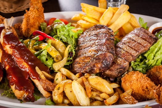 Huge barbecue plate with mixed meat and steaks on salad