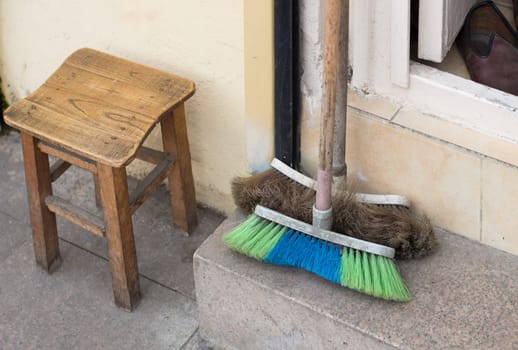 two old brooms next to small wooden stool