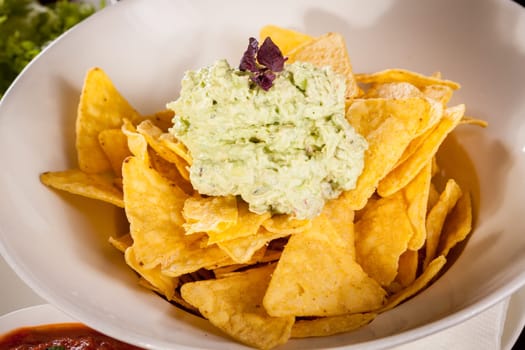 Corn chips nachos with guacamole and salsa dipp in a bowl on a plate