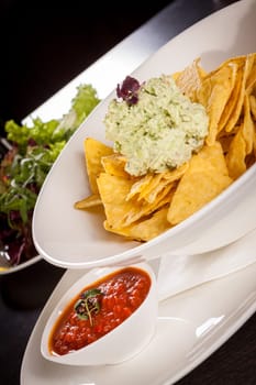 Corn chips nachos with guacamole and salsa dipp in a bowl on a plate