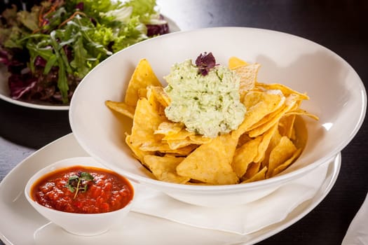 Corn chips nachos with guacamole and salsa dipp in a bowl on a plate