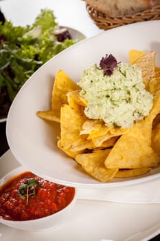 Corn chips nachos with guacamole and salsa dipp in a bowl on a plate