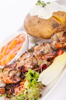 Roasted shrimp on a skewer on mixed salad with dip and foil potato prepared on a plate insulated against a white background