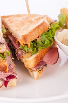 Delicious sandwich clubsandwich with bacon ham cheese and one with mixed pickels on a plate isolated against a white background